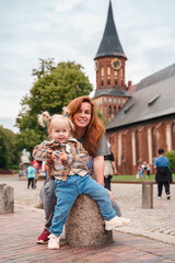 Wall Mural - A little Caucasian toddler girl with a young mother travels in Kaliningrad near the Cathedral in the city center.