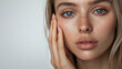 © Bonsales - Close up of young woman with clear skin and freckles touching her face. Natural beauty, soft skin texture, and expressive eyes