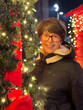 © satura_ - Cheerful woman poses amidst festive lights and decorations, capturing the warmth and joy of holiday Christmas season. Surrounding glowing elements and their bright smile create an inviting and cozy