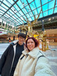 © satura_ - Joyful moment captured as mother and daughter stand in front of a dazzling golden reindeer sculpture, showcasing festive decorations in modern mall setting. Christmas holiday cheer and warmth
