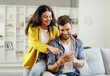 © Home-stock - Happy young indian couple using smartphone, wife pointing at cellphone screen, sitting on sofa in living room interior at home. New app ad, banner