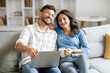 © Home-stock - Happy hindu spouses resting together with laptop and coffee, relaxing in cozy living room on sofa, man and woman chatting and using computer