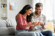 © Home-stock - Happy indian spouses holding positive pregnancy test, sitting on couch at home together, couple celebrating awaiting baby, copy space