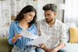 © Home-stock - Indian couple checking bills, reading documents, unhappy man and woman holding papers