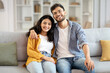 © Home-stock - Loving indian spouses embracing, sitting on sofa in modern living room, husband hugging his wife and beaming with smiles together at camera