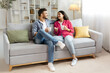© Home-stock - Happy indian couple relaxing and drinking coffee, sitting on couch at home, talking , free space
