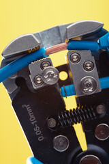 Close-up of a wire stripper tool cutting a blue wire with exposed copper. Macro shot of electrical equipment.