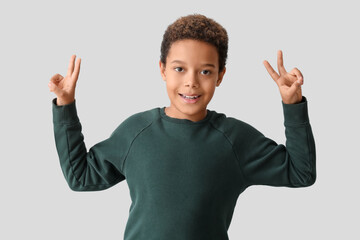 Canvas Print - Little African-American boy showing victory gesture on white background