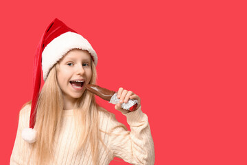 Poster - Cute little girl eating chocolate Santa Claus on red background