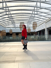 Millennial woman poses confidently in an open, modern environment, wearing a vibrant red sweater and black boots. Joyful expression captures a sense of freedom and individuality