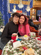 © satura_ - Mother and daughter sit together at a festively Christmas decorated table, surrounded by holiday lights and ornaments in cozy cafe. Enjoying warm drinks, showcasing a joyful and celebratory atmosphere