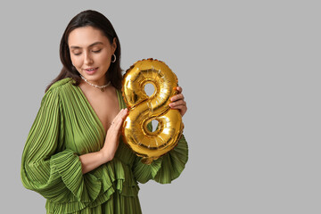 Poster - Beautiful young woman with golden air balloon in shape of figure 8 on grey background. International Women's Day