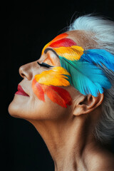 Wall Mural - A senior Brazilian woman with vibrant, colorful feathers painted across the side of her face, set against a black background, merging bold beauty with an elegant profile.