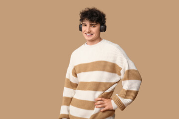 Wall Mural - Handsome young man in stylish sweater and headphones on brown background