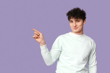 Wall Mural - Handsome young man in stylish white sweatshirt pointing at something on purple background