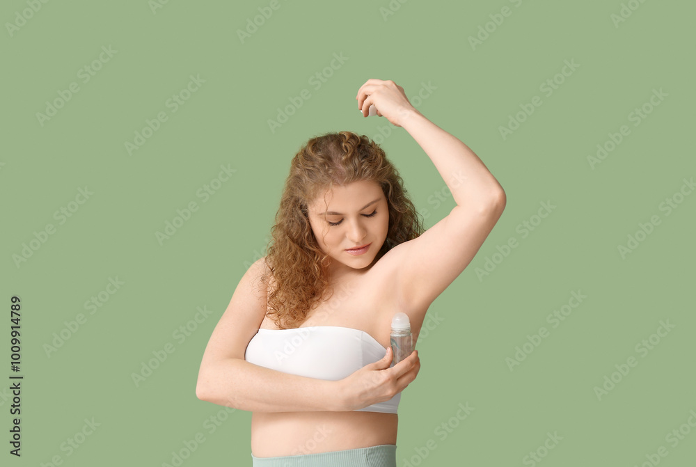 Beautiful young woman applying deodorant on green background