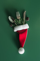 Santa hat with silver cutlery and Christmas decoration on green background. Christmas dinner concept design. 3D Rendering, 3D Illustration