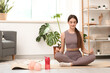 © Pixel-Shot - Sporty young woman with bottle of water meditating on fitness mat at home