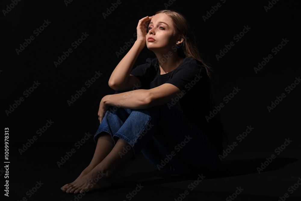 Crying young woman sitting on black background
