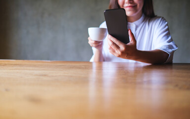 Poster - Closeup image of a young woman holding and using mobile phone while drinking coffee in cafe