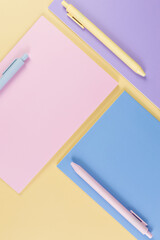 Wall Mural - Top view of pink, purple and blue notebooks on yellow background. Pink, yellow and blue pens, school, office wallpaper. Flat lay, copy space.