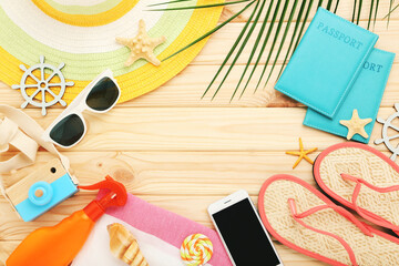 Wall Mural - Flip flops, straw hat, seashells, passports, towels and palm leaf on brown wooden background