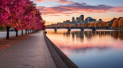 Poster - A Tranquil Cityscape With A Bridge Spanning Over A Calm River In Front Of A Colorful Autumnal Skyline