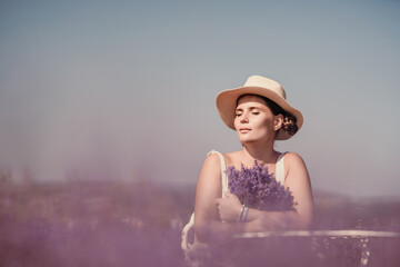 Canvas Print - woman sitting in a field of lavender and wearing a straw hat. She is smiling and holding a bouquet of flowers. Scene is peaceful and serene, as the woman is surrounded by the beauty of nature