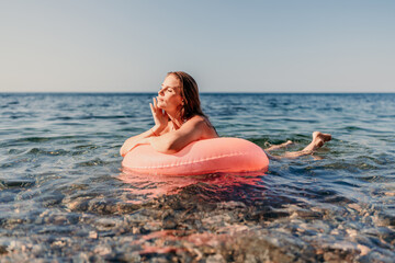 Canvas Print - A woman is floating on a pink inflatable ring in the ocean