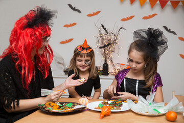 mom and two kids daughters in masquerade costumes  paint gingerbread for the halloween holiday at home. Halloween party
