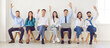 © Studio Romantic - Young cheerful colleagues and company employees raising hands to vote at conference sitting on chairs in row in meeting room. Smiling business people men and women voting in office during a meeting