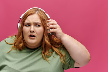 A woman with red hair adjusts her headphones while looking off to the side.