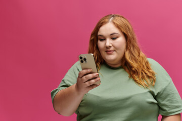 A woman in a green t-shirt looks intently at her phone, her expression focused.