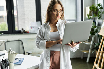 A woman uses a laptop while standing in an office.