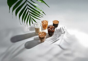 Poster - Four iced coffee drinks in glass cups on a white surface with palm leaf shadows.