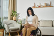 © Bliss - A woman sits in a wheelchair in a living room, reading a book.