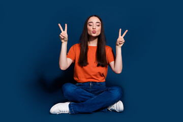 Wall Mural - Photo of lovely nice pretty cheerful woman wear orange stylish clothes sit floor v-sign isolated on dark blue color background