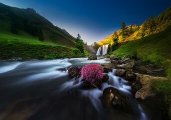Poster - A rushing stream flows through a mountainous landscape, a waterfall cascading in the distance, and vibrant pink flowers blooming near the edge.