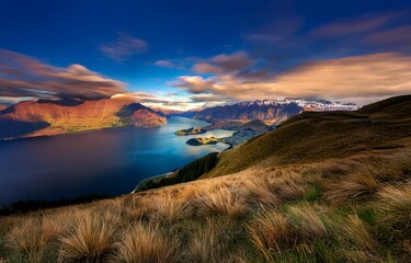 Poster - A breathtaking view of a valley, with a vast lake surrounded by mountains. The sky is filled with dramatic clouds, and a small town is nestled at the base of the mountains.