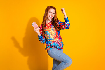 Wall Mural - Photo portrait of attractive young woman hold device winning dressed stylish colorful clothes isolated on orange color background