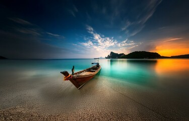 A wooden boat rests on a sandy shore,  with calm, turquoise waters and an orange sunset in the background.