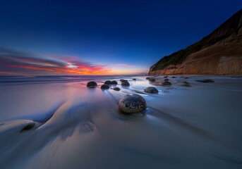 Aufkleber - A scenic New Zealand landscape with smooth, round stones scattered on the beach at sunset.