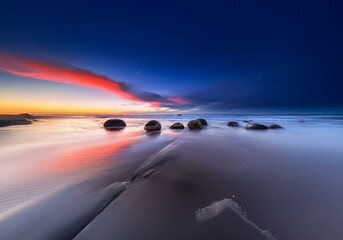 Aufkleber - A beautiful sunset over a New Zealand beach with large round boulders on the shore.