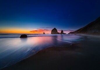 Aufkleber - A New Zealand landscape featuring a dramatic sunset over a serene ocean with rock formations in the distance.