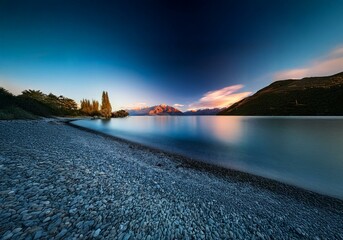 Poster - A serene New Zealand landscape with a calm lake, mountains in the distance, and a pebble beach in the foreground.
