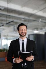 Wall Mural - A man in a suit holding a book and a pencil. He is smiling and he is happy