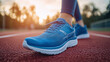 © Oleksandr - Close-up of a person wearing blue athletic running shoes on a red track at sunset. Focus on the shoe detailing and texture, with a blurred background