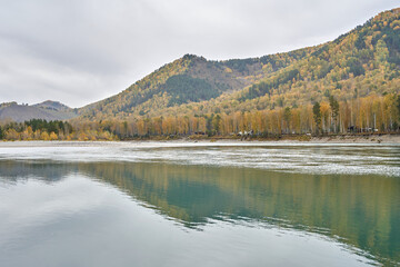 Tranquil autumn lake scene with reflected mountains and vibrant forest in serene landscape.