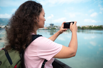 Woman capturing scenic lake view with smartphone outdoors