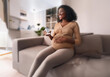 © YiuCheung - A pregnant woman sits on a couch, smiling and holding a glass jar of pills.